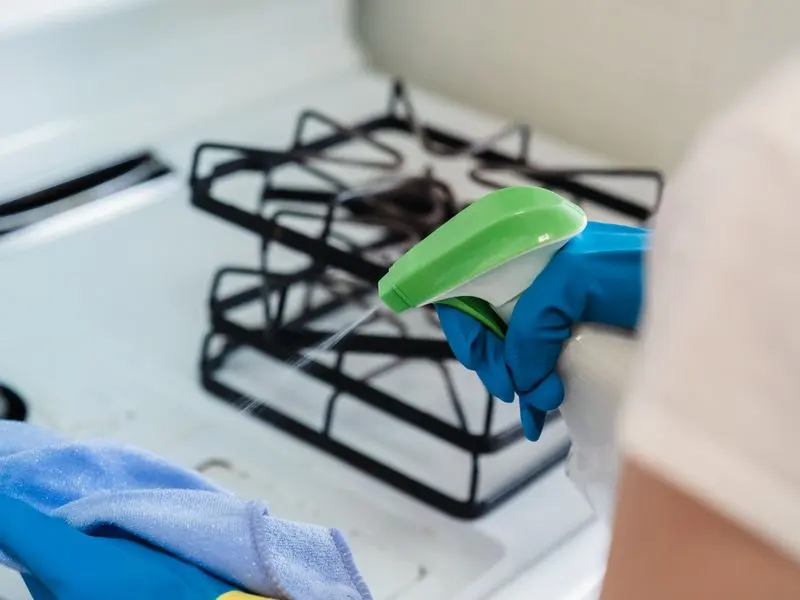 Gloved hand cleaning a kitchen stove with spray and a cloth