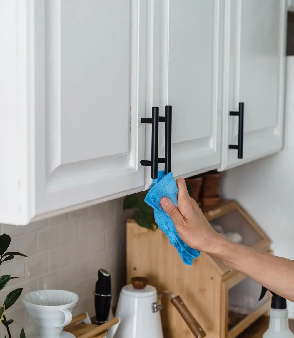 Blue cloth cleaning white kitchen cabinet doors